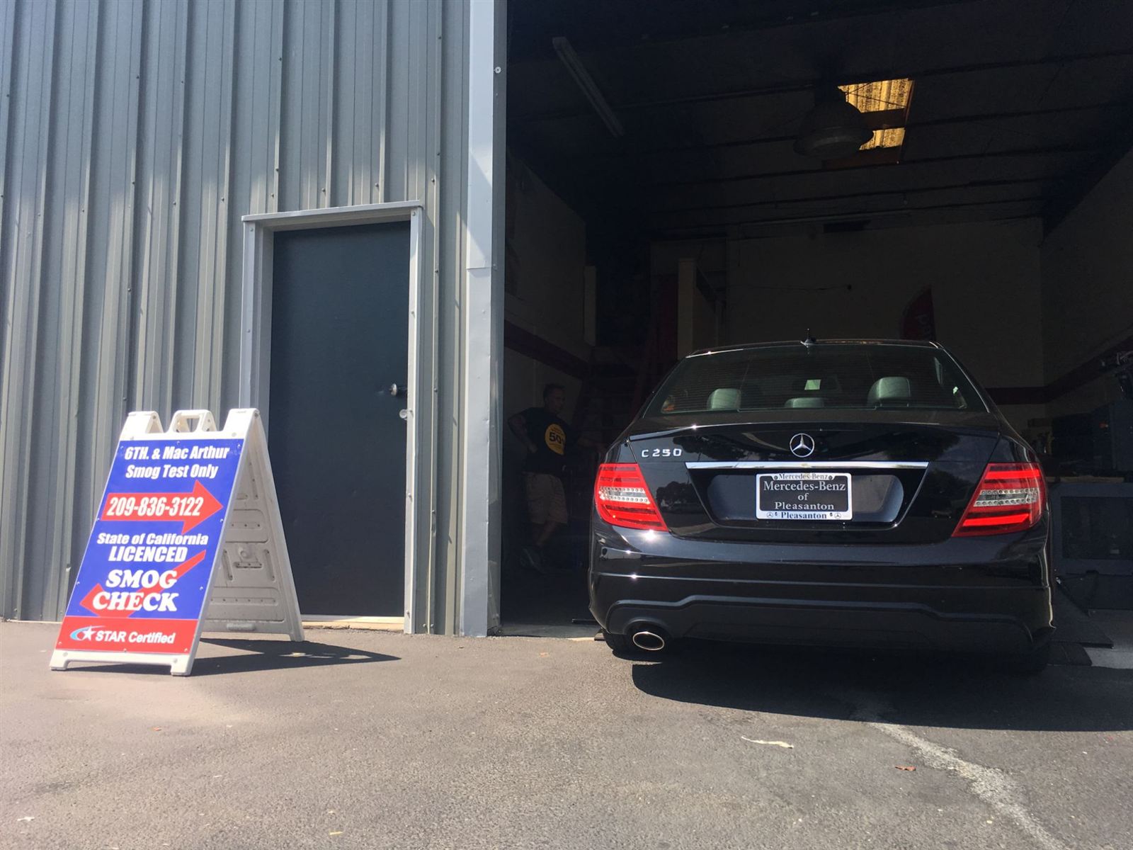 Smog check sandwich-board sign and open test bay with a vehicle being inspected at 6th St. & MacArthur Smog in Tracy